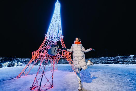 a girl in a gray jacket in winter with evening lights burning on Christmas street.