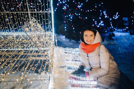 a girl in a gray jacket in winter with evening lights burning on Christmas street.