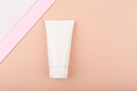 Creative elegant flat lay with white cream tube with face or hand cream or lotion on bright pastel beige background decorated with white and pink paper. Concept of beauty products for skin care