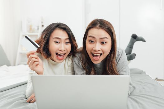 Asian woman friends sitting in living room using digital tablet for online shopping with credit card together