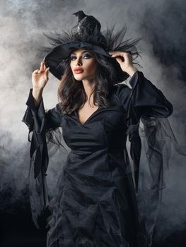 Beautiful woman in Halloween witch costume dress and hat in mist