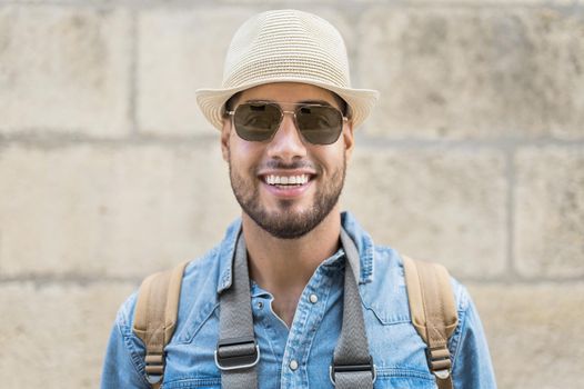 Close up shot of handsome man traveler having nice walk in old town during summer vacations. Man wearing stylish mirrored lens sunglasses and hat standing in urban setting. High quality photo