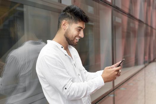 Young handsome men using smartphone in a city. Smiling young man texting on his mobile phone. Coffee break. Modern lifestyle, connection, business concept. High quality photo.