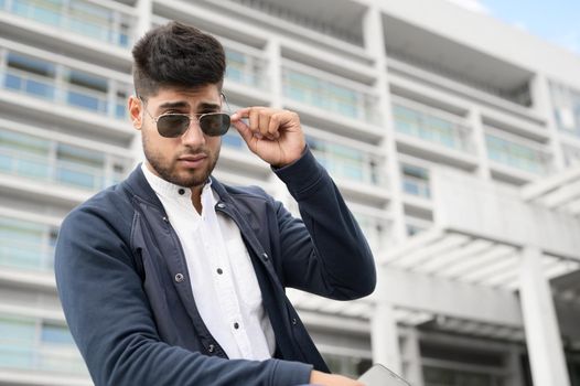 Portrait of young man in stylish sunglasses posing near modern building. High quality photo