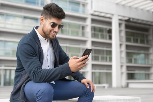 Young handsome men using smartphone in a city. Smiling young man texting on his mobile phone. Coffee break. Modern lifestyle, connection, business concept. High quality photo.