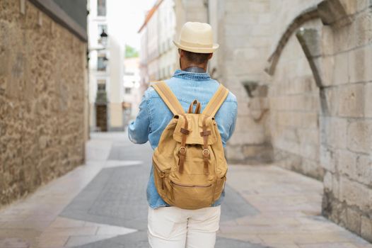 Rear view of a young man with backpack walking on the street in the old town. High quality photo.