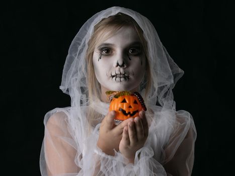 Little girl in Halloween ghost costume holding halloween pumpkin basket with worm candies, studio isolated on black background