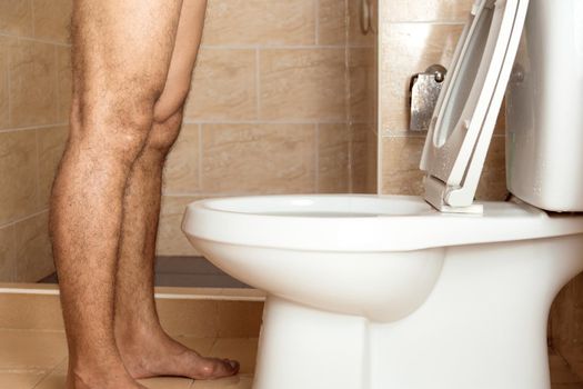 Close-up of the legs of a man standing urinating in the toilet.