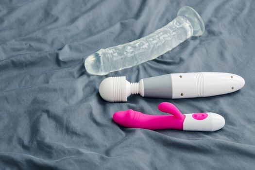 Close-up group of various sex toys lying on a crumpled mattress.