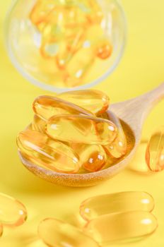 Fish oil capsules in wooden spoon on yellow background.