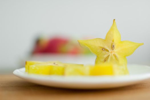 Exotic starfruit or averrhoa carambola on white plate on wooden cut board. Healthy food, fresh organic star apple fruit