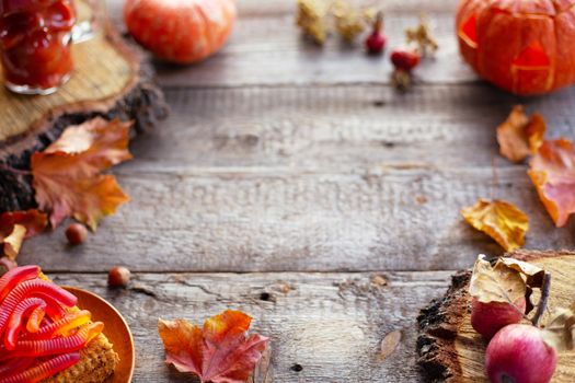 Halloween food still life abstract background with pumpkins, apples, cake, gummy worms, skull red drink and candles