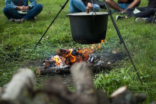 Dark big pot or cauldron, cooking pan with boiling water inside above the fire somewhere in the park or mountains, camping concept.
