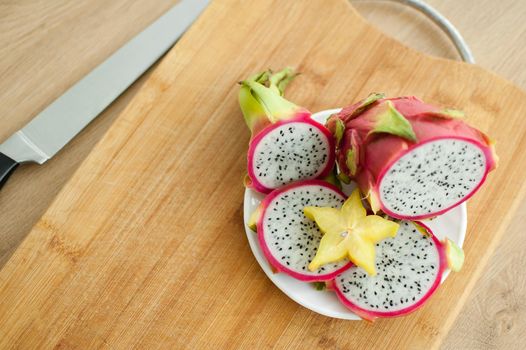 Slices of dragon fruit or pitaya with white pulp and black seeds on white plate with one slice of starfruit or averrhoa carambola. Exotic fruits, healthy eating concept.