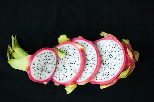 Slices of dragon fruit or pitaya with pink skin and white pulp with seeds on black background. Exotic fruits, healthy eating concept.