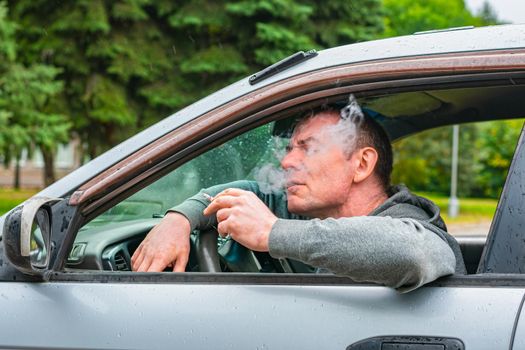 The driver smokes and enjoys a cigarette while driving his car, thereby harming his health