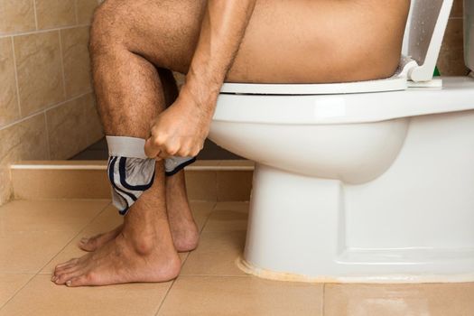 Close-up of a man's legs sitting stool on the toilet bowl.