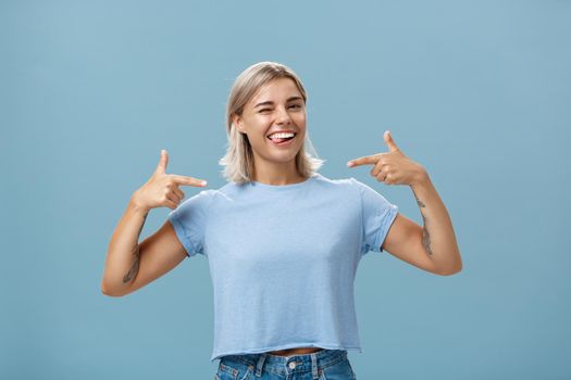 Girl proudly indicates at herself bragging with own achievements. Ambitious creative and smart attractive woman with tanned skin smiling joyfully sticking out tongue and winking pointing at chest.