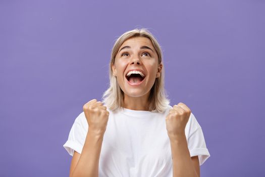 Waist-up shot of grateful delighted lucky girl with attractive tan in white t-shirt clenching fist from positive emotions gazing delighted and happy up thankful giving thanks god for fulfilling dream. Emotions concept