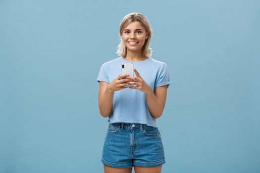 New phone is fantastic. Portrait of satisfied happy young modern blond woman in trendy outfit with blond short haircut smiling joyfull from delight holding smartphone near chest texting or using apps. Technology concept