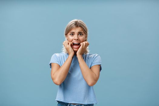 Lifestyle. Indoor shot of shocked troubled girlfriend hearing mom returned home being with boyfriend biting fingernails being in helpless perplexed situation feeling anxious and scared over blue background.