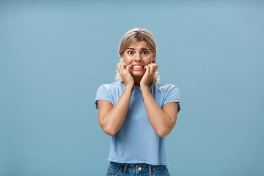 Gosh scary movies makes me tremble. Portrait of worried young attractive and stylish woman starting panic and nervous clenching teeth holding hands near mouth and frowning looking concerned and scared.