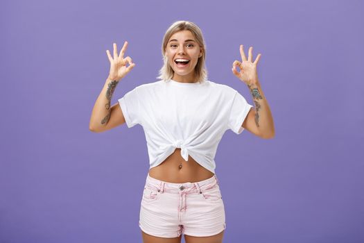 Girl being agree with friends deciding were enjoy holidays. Portrait of charming satisfied and happy young blonde female with tattoos and pierced belly showing okay gesture and smiling with delight. Copy space