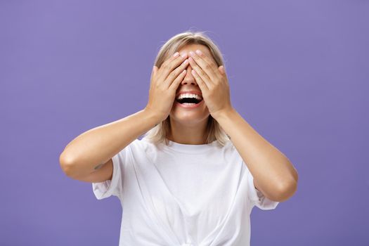 Can I look now. Portrait of excited pleased attractive tanned girlfriend in white t-shirt closing eyes and smiling broadly waiting for boyfriend bring surprising gift over purple background.