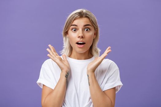 Lifestyle. Close-up shot of charmed and impressed good-looking caucasian girlfriend with blond hair and tattoos on arms raising hands in amazed and excited gesture opening mouth and gazing mesmerized at camera.