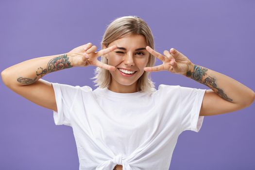 Say cheeze. Portrait of joyful sociable and popular good-looking stylish woman with cool tattoos on arms showing peace or disco moves over eyes winking and smiling broadly feeling awesome. Emotions concept