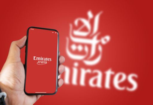 Dubai, UAE, July 2021: A hand holding a phone with the Emirates airline app on the screen and the Emirates logo Blurred on a green background.