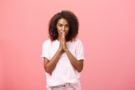 Creative and smart stylish attractive african american woman with curly hairstyle having great plan or idea feeling ambitious holding hands in pray over mouth gazing thoughtful at camera. Copy space