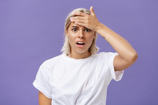 Girl totally forgot about important meeting feeling troubled. Concerned worried good-looking young employee with tanned skin and fair hair holding hand on forehead and frowning from anxiety. Copy space