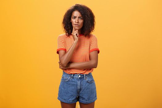 Woman looking concerned picking new furniture in store. Thoughtful focused and troubled smart african american businesswoman in casual outfit frowning biting lip touching mouth while thinking.