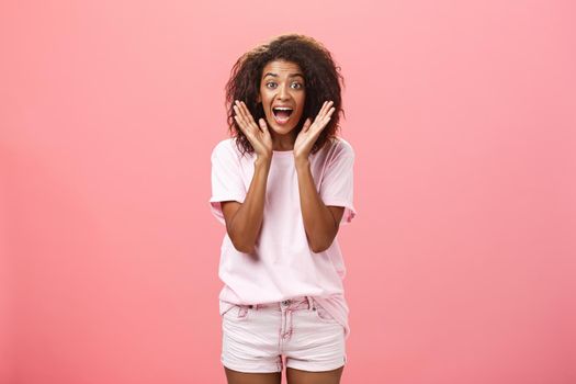 Indoor shot of expressive excited attractive dark-skinned adult woman in casual outfit yelling from amazement and joy holding palms near face reacting on awesome news with excitement and happiness. Lifestyle.