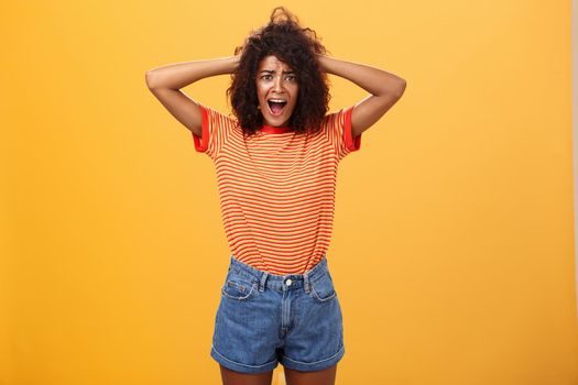 Girl panicking not being ready meet boyfriend parents. Portrait of shocked troubled and concerned gloomy girlfriend with afro hairstyle holding hands on hair yelling from shock over orange background. Copy space