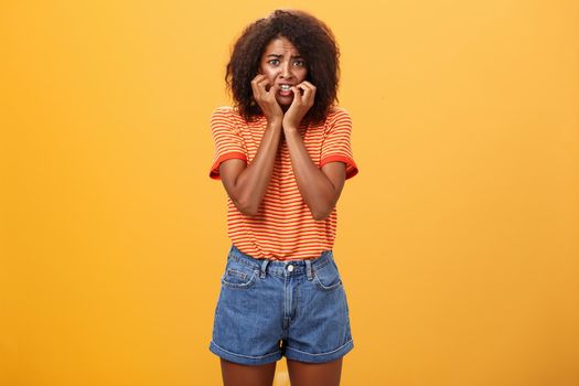 Woman feeling empathy for boyfriend got in trouble standing nervous over orange background biting fingernails frowning and panicking being scared and shocked over orange background. Copy space