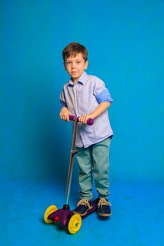 A boy on a scooter on a blue background . An article about children's scooters. An article about the choice of a scooter for a child. A happy child. Blue background and a boy. Copy Space