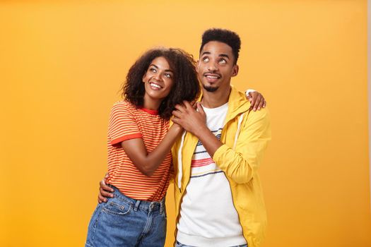 Couple of lovers enjoying spending warm summer evening together gazing up at stars with happy. enthusiastic expression being in love hugging and expressing warm romantic feelings over orange wall.