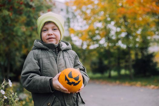 A boy with a Halloween pumpkin with eyes . The feast of fear. Halloween. An orange pumpkin with eyes. An article about Halloween.