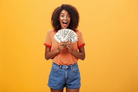 Woman cannot hide happiness winning lottery. Portrait of surprised and happy lucky african american young woman with curly hair holding bunch of money and yelling from delight receiving paycheck. Copy space