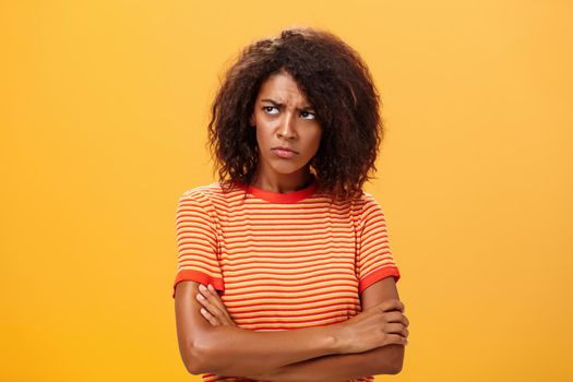 Why life so cruel and unfair. Gloomy displeased and sad cute african american young woman with curly hairstyle crossing arms on chest in offended pose frowning looking left jealous and unhappy.