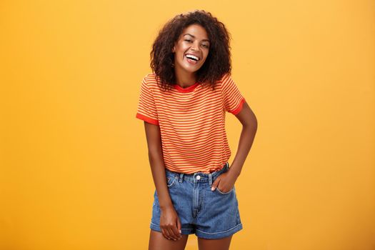 Portrait of charismatic charming african american stylish african american female in trendy shorts and t-shirt laughing happily enjoying talking with cool people laughing posing over orange background. Lifestyle.