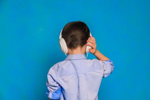 A boy with headphones on a blue background . Children's headphones. Harm of headphones for the child. Useful audiobooks for children. An article about children's leisure. Music. Copy Space