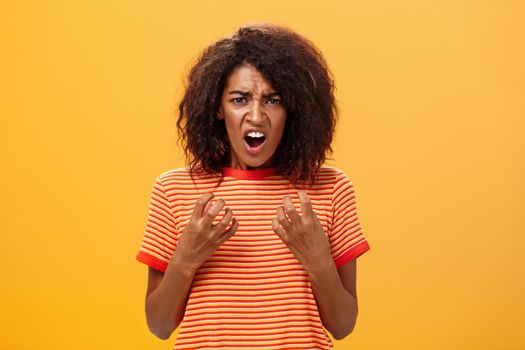 Waist-up shot of woman feeling upset feeling unfair things happened complaining and whining with regret frowning gesturing with palms near breast standing over orange background. Copy space