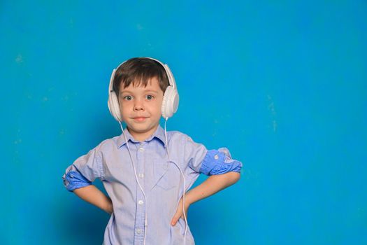 A boy with headphones on a blue background . Children's headphones. Harm of headphones for the child. Useful audiobooks for children. An article about children's leisure. Music. Copy Space