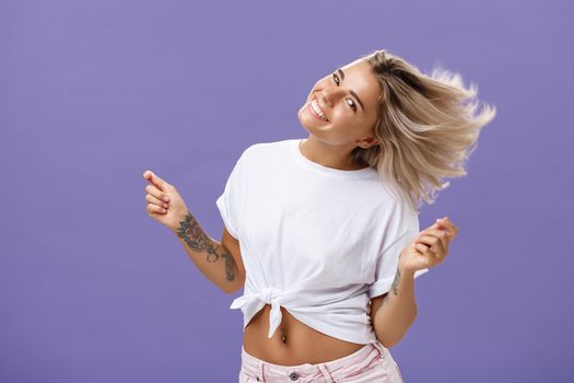 Portrait of happy carefree attractive woman dancing and waving hair from rejoice and cheer smiling broadly tilting head celebrating end or working day enjoying nice sunny day on beach over purple wall. Emotions and lifestyle concept