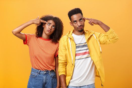 Pair of african american lovers getting annoyed with parents scolding, teaching them how live sexual life rolling eyes up from irritation holding finger gun near temples standing close to each other. Relationship concept