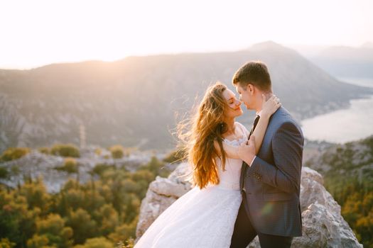 A bride and a groom are hugging on the mount Lovcen, a panoramic view of the Bay of Kotor opens in front of them . High quality photo