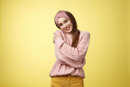 Girl feeling warm and safe thanks charming boyfriend embracing herself romantically hugging leaning on shoulder enjoying warmth of fluffy sweater, smiling tender in love over yellow background.